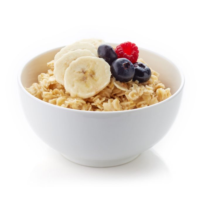 Ciotola di cereali bio con fette di banana, mirtilli e lampone per una colazione sana.